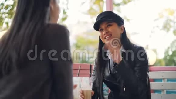快乐的亚洲女孩在街边咖啡馆和她的女朋友聊天然后用鸡尾酒敬酒和碰杯视频的预览图