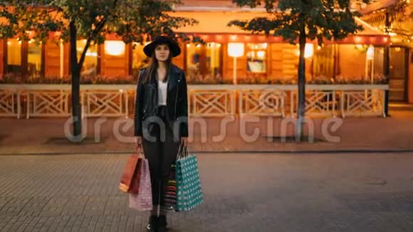 在繁忙的街道上穿着时髦服装的漂亮女孩拿着购物袋站在那里看着摄像机从而缩短了时间视频的预览图
