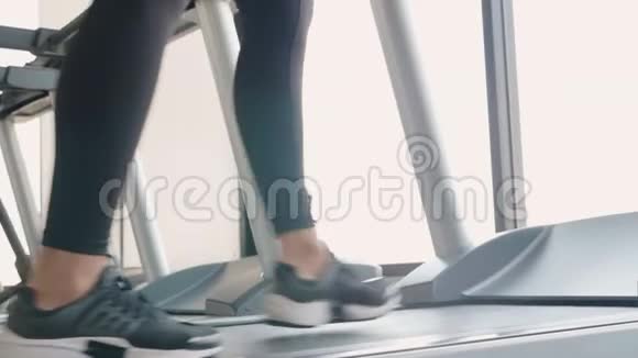 在健身运动健身中心的跑步机上用运动服跑步和慢跑将运动型女孩的腿收起来视频的预览图