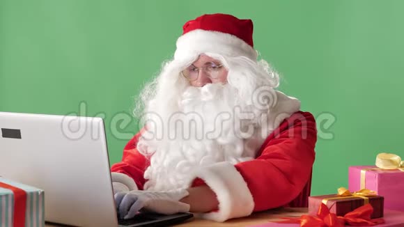 严肃的圣诞老人坐在笔记本电脑上打印办公室工作人员绿色的背景视频的预览图