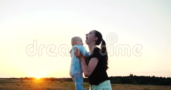 快乐的母亲扎着马尾辫在夕阳西下的大片田野里抚养孩子视频的预览图