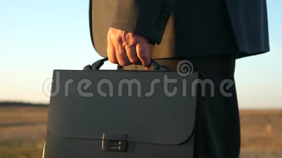 夏天一个农夫手里拿着一个黑色公文包穿过田野特写镜头穿西装的商人走路视频的预览图