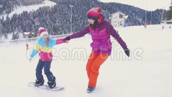 母亲帮助女儿在滑雪坡上正确地骑在滑雪板上寒假概念视频的预览图