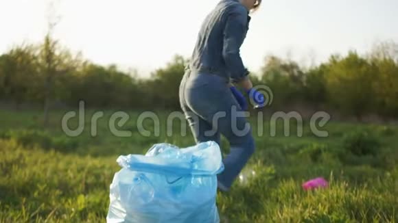 止塑社会观念穿牛仔裤的女孩在公园里用一个蓝色的大塑料袋收集垃圾视频的预览图