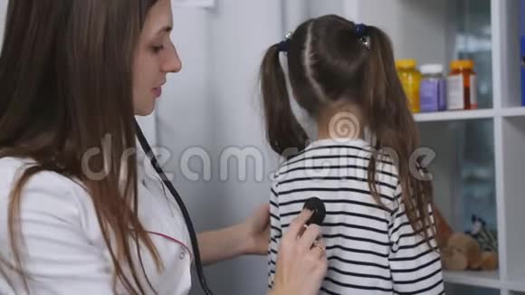 女医生在一家医疗诊所的办公室里听着带音响镜的小女孩说话视频的预览图