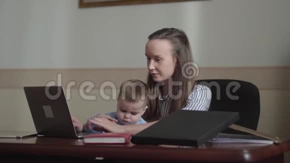 一个可爱的女商人带着婴儿和笔记本电脑在办公室工作视频的预览图