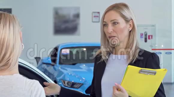 在汽车经销商沙龙工作的成熟的女销售员与客户交谈视频的预览图