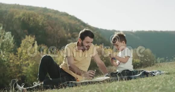 有魅力的人和他的儿子在大自然中玩耍躺在草地上一起度过一段有趣的时光视频的预览图