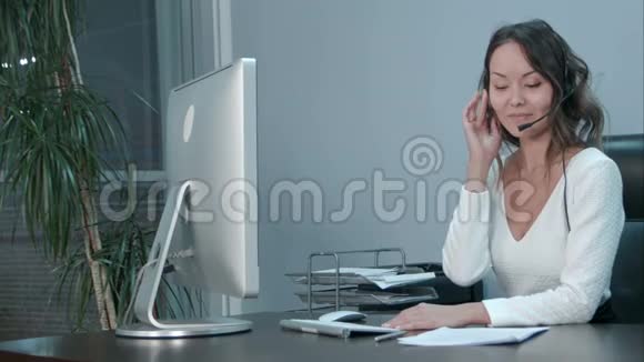 友好的亚洲年轻女性接线员在现代办公室带耳机的笔记本电脑上工作视频的预览图