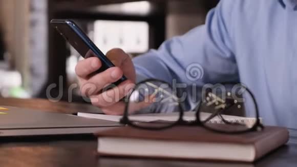盖伊的特写手里拿着一个电话桌子上有一个笔记本电脑眼镜和一个笔记本视频的预览图