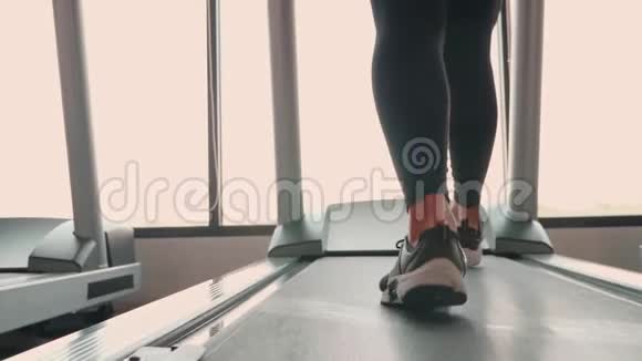 在健身运动健身中心的跑步机上用运动服跑步和慢跑将运动型女孩的腿收起来视频的预览图
