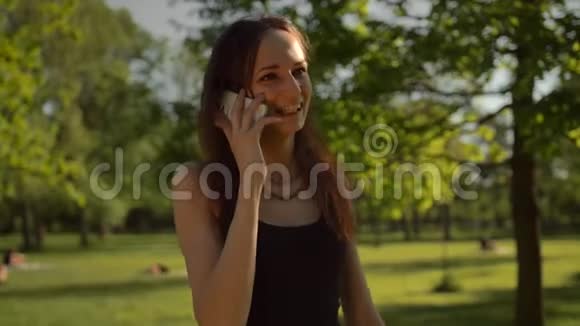 微笑的年轻女士站在公园外面打电话视频的预览图