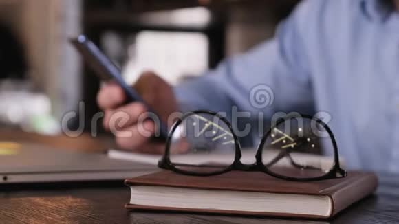 盖伊的特写手里拿着一个电话桌子上有一个笔记本电脑眼镜和一个笔记本视频的预览图