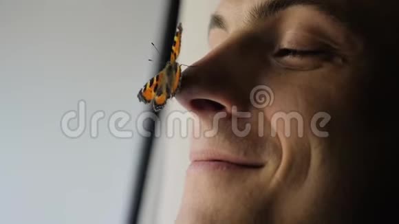一只美丽的蝴蝶坐在一个年轻人的鼻子上那家伙微笑着蝴蝶扇动翅膀视频的预览图
