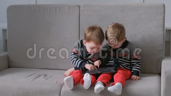 两个孪生兄弟坐在沙发上平板带走了对方孩子们在平板电脑上玩游戏视频的预览图