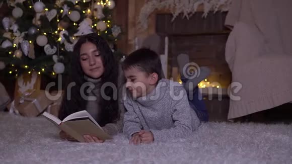 在圣诞节妈妈给儿子读了一本书吻了他躺在圣诞树附近的地板上4K视频的预览图