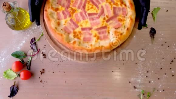 厨师戴着橡胶手套把培根比萨饼放在桌上的木板上双手特写视频的预览图