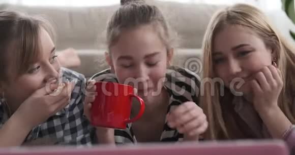 女孩一边吃东西一边喝东西一边看笔记本电脑上的媒体内容视频的预览图