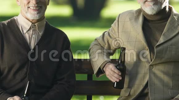 微笑的老年人展示啤酒瓶坐在长凳上不含酒精的饮料视频的预览图