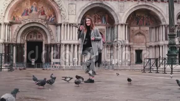 快乐美丽的女游客手里拿着智能手机和鸽子在意大利威尼斯圣马可广场慢动作视频的预览图