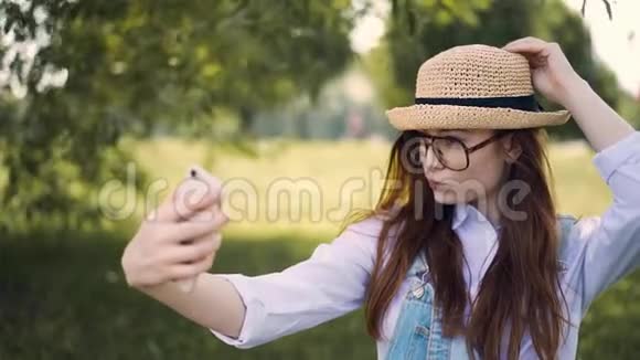 戴着眼镜和草帽的生姜女孩在公园里自拍摸她的头发视频的预览图
