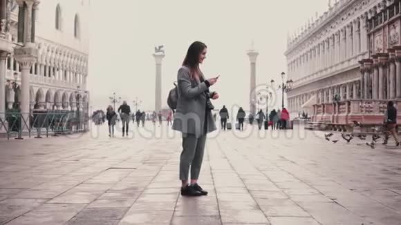 快乐微笑的旅游女孩在意大利威尼斯城市广场拍摄鸽子群的智能手机照片视频的预览图
