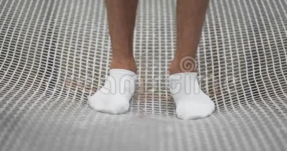 白色袜子的脚特写在蹦床网格上摆动以缓慢的运动跳跃演讲的开始视频的预览图