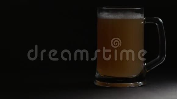 明亮的大玻璃杯与冷啤酒周围的聚光灯隔离在黑色背景视频的预览图