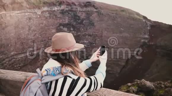 年轻快乐的自由职业者女孩背着背包在意大利度假时拍摄维苏威火山口的智能手机照片视频的预览图