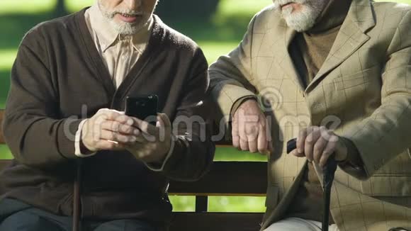 带着手杖的老人给朋友看智能手机照片现代科技视频的预览图