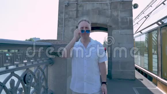 一个穿着白色衬衫和太阳镜的中年男子站在桥上视频的预览图