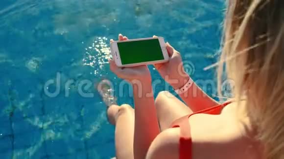 女孩使用水平手机绿色屏幕同时放松附近的游泳池手握智能手机镀铬视频的预览图