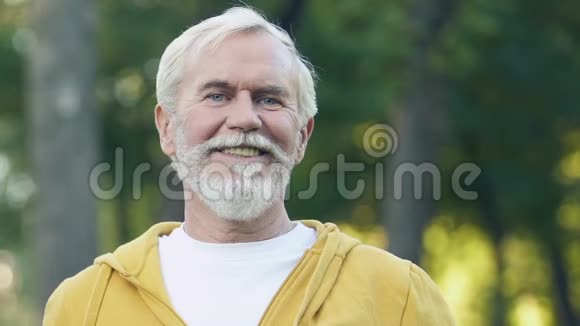 灰发男子对着镜头微笑花时间在新鲜空气上做体操视频的预览图