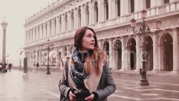 美丽的女性旅行博主用相机拍摄意大利威尼斯圣马克建筑的照片微笑慢动作视频的预览图