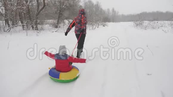 快乐的爸爸在雪地的路上载着一个孩子圣诞节假期父亲和女儿在冬天的公园里玩这就是视频的预览图