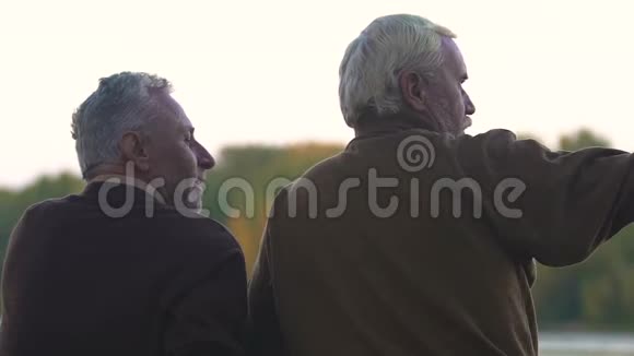 成熟的男人给他的朋友讲故事指着坐在海岸上的远方视频的预览图