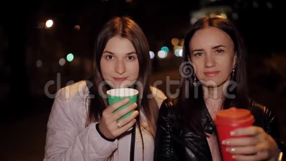 两个微笑的朋友晚上在街上的肖像手里拿着咖啡视频的预览图