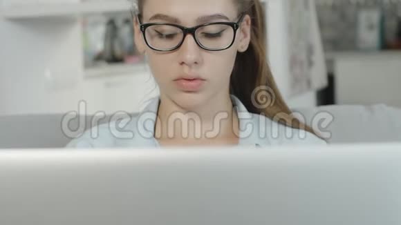 戴眼镜的十几岁女孩看着笔记本电脑上的文字看着笔记本屏幕视频的预览图