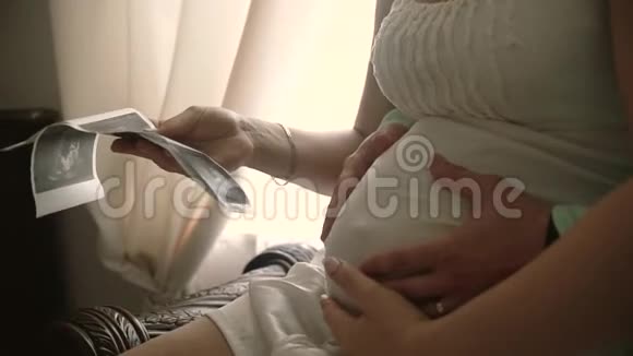 一对夫妇在沙发上看婴儿的超声波扫描慢动作视频的预览图