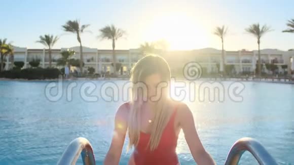 在炎热的阳光明媚的一天穿着湿红泳衣走出蓝色游泳池的迷人年轻女子特写肖像视频的预览图