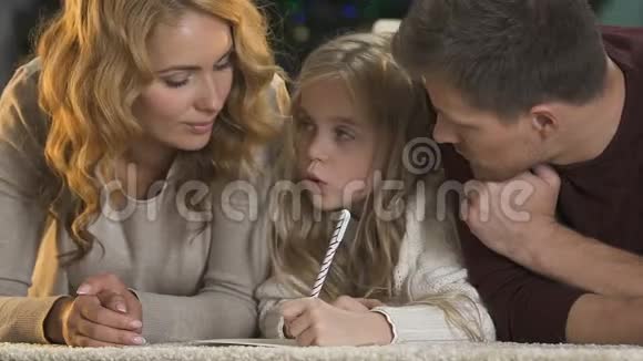 美丽的家庭躺在地板上父母帮助小女儿写祝福视频的预览图