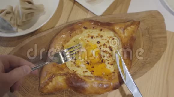 男性手拿着一块食物用叉子靠近卡查普里格鲁吉亚奶酪派和鸡蛋在咖啡馆的木板上视频的预览图