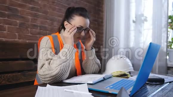 穿着橙色头盔和橙色背心的女建筑工人在房间里的笔记本电脑上工作视频的预览图