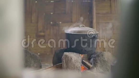 在木制墙壁背景上的篝火上煮食物在亚洲传统的水壶里准备晚餐视频的预览图