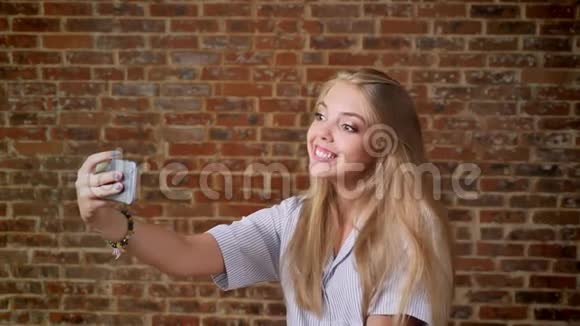年轻的白种人金发女郎自拍笑微笑照片智能手机肖像砖墙的背景视频的预览图