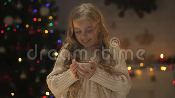 女孩拿着一个杯子杯子里放着热巧克力靠近发光的圣诞灯视频的预览图