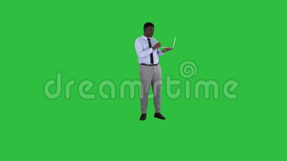 与照相机交谈年轻的非洲男子手拿笔记本电脑在绿色屏幕Chroma键视频的预览图