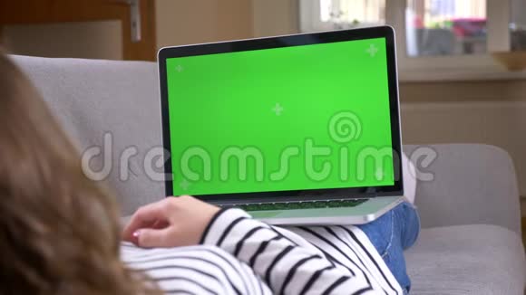 笔记本电脑上女性观看广告的特写后景拍摄绿色屏幕躺在室内沙发上视频的预览图