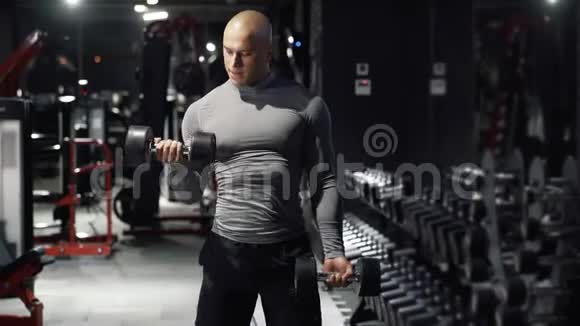 强壮的肌肉男用哑铃做运动锻炼在黑暗的健身房训练二头肌手部肌肉一项运动视频的预览图