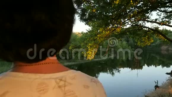 一个年轻的女人站在森林和河流背景上的一棵树附近特写镜头视频的预览图